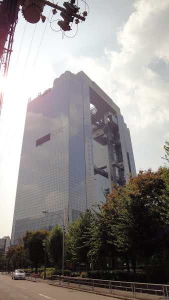 umeda sky building from a distance.  There are two rectangular glassed towers connected by a walkway close to the highest floors and a rooftop canopy with a large open space in the center